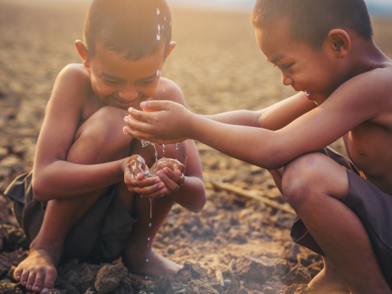 two boys sitting in sand playing with water